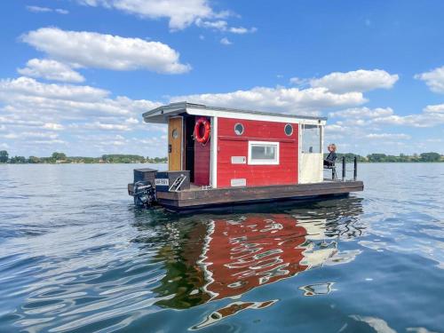 une maison rouge sur un bateau dans l'eau dans l'établissement Hausfloßvermietung auf der Peene am Kummerower See in Mecklenburg Vorpommern, à Dargun