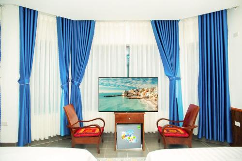 um quarto com cortinas azuis e uma televisão e duas cadeiras em Tam Coc Center Boutique Hotel em Ninh Binh