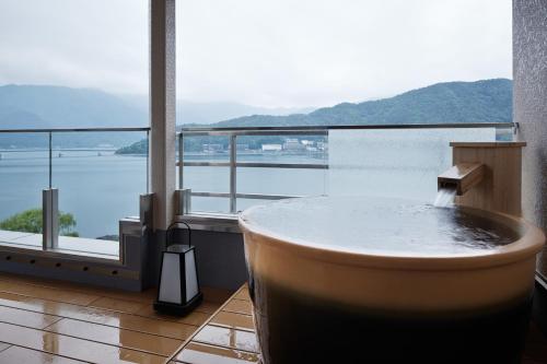 a bath tub in a room with a large window at Fujikawaguchiko Onsen Konanso in Fujikawaguchiko