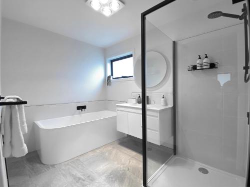 a white bathroom with a bath tub and a sink at Albatross Rise - Modern Family Home in Hobart