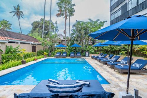 una piscina con tumbonas y sombrillas azules en Villa Coco Bali, en Seminyak