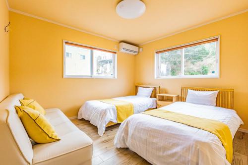 a room with two beds and a couch and two windows at ふくろう庵-白浜- in Shirahama