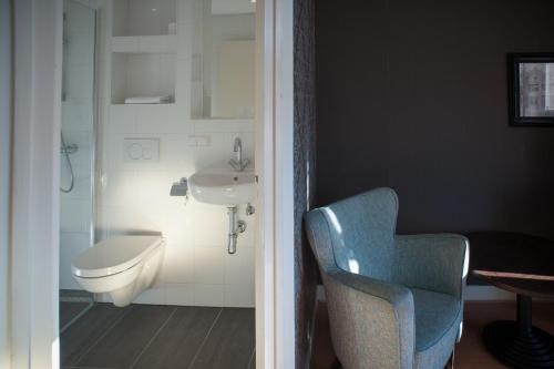 a bathroom with a sink and a toilet and a chair at Hotel Grand Cafe Deight in Zandvoort
