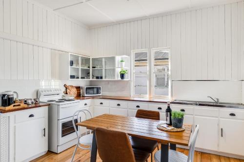 a kitchen with white cabinets and a wooden table at Cheerful, Cosy Cottage - Near Rose Garden! in Toowoomba