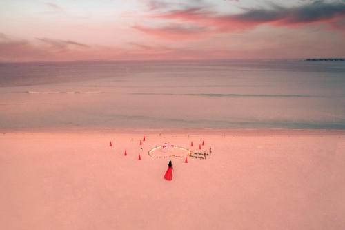 a woman in a red dress walking on a beach at Hideaway Beach Resort & Spa, FREE SHARED CHARTER FLIGHT for two on stays of 7 or more nights from September 2025 until 23rd December 2026 in Dhidhdhoo