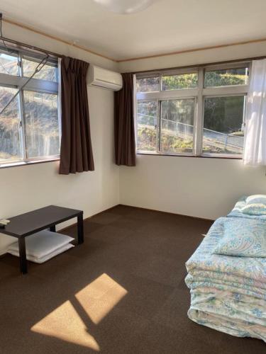 um quarto com uma mesa, um sofá e janelas em Guest House Iwato em Takachiho