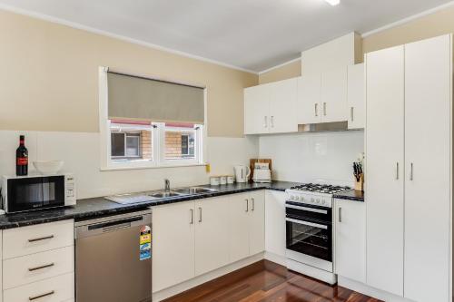 uma cozinha com armários brancos e um forno com placa de fogão em Light & Bright! 3 Bedroom Cottage, East Toowoomba! em Toowoomba
