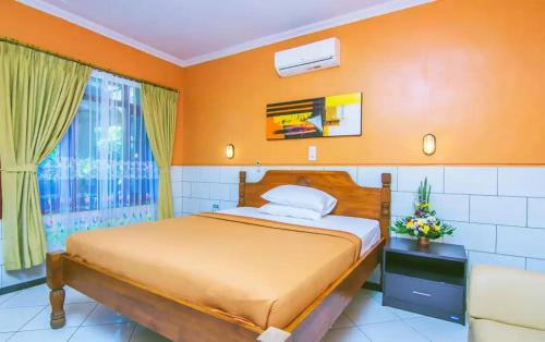 a bedroom with a bed with orange walls and a window at Kedin's Inn in Denpasar
