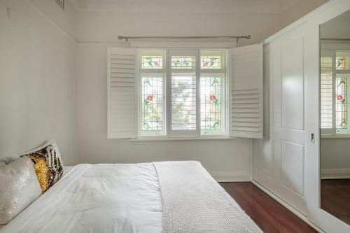 a bedroom with white walls and windows and a bed at Elegant Federation Home Near The Airport in Sydney