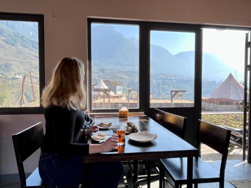 a woman sitting at a table looking out the window at S Plus Bungalow in Sa Pa