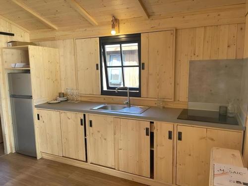 une cuisine avec des armoires en bois, un évier et une fenêtre dans l'établissement Camping Le Gallo Romain, à Barbières