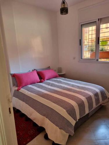 Un dormitorio con una cama con almohadas rosas y una ventana en Pied à terre proche aéroport, en Marrakech