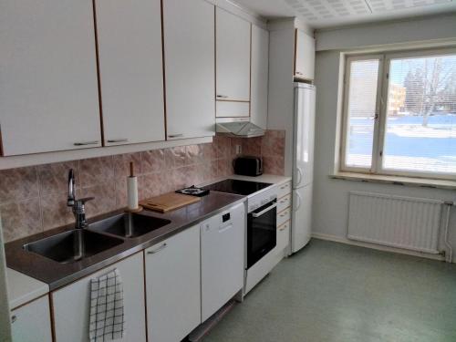 cocina con armarios blancos, fregadero y ventana en Kuhmoisten Kivilinna, en Kuhmoinen