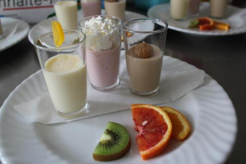 three glasses of milkshakes on a white plate with fruit at Landgasthof Weberhans in Harburg