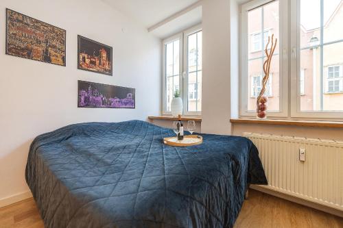 a bedroom with a bed with a blue blanket and windows at Hello Apartments Modern Studio Sw Ducha in Gdańsk