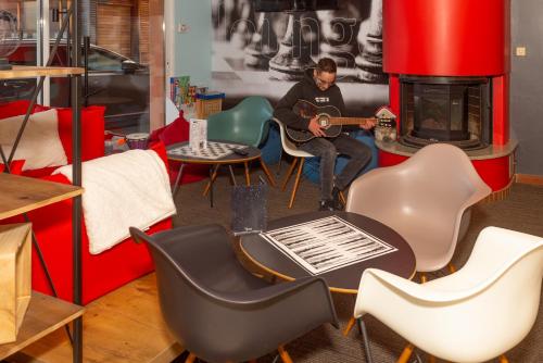 a man playing a guitar in a room with chairs at ibis La Bresse Gérardmer in La Bresse