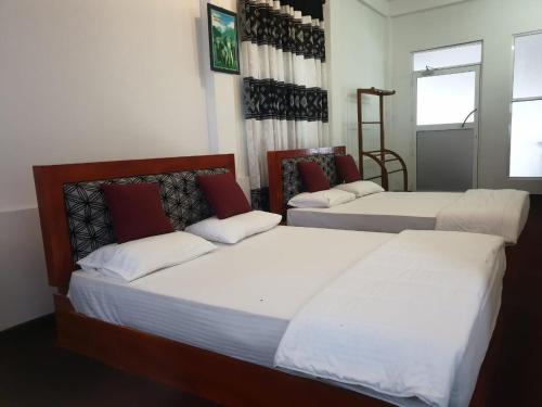 a bedroom with three beds with white and red pillows at Relax Lake View Resort in Kataragama