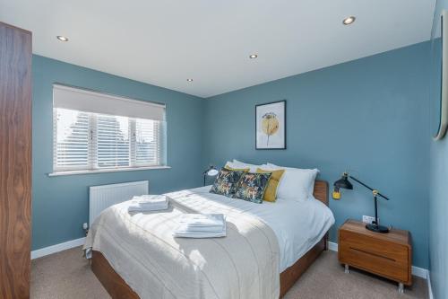 a blue bedroom with a large bed and a window at Castle Townhouse Kenilworth - Private Parking - 24 Hr Gym Access - Town Centre in Kenilworth