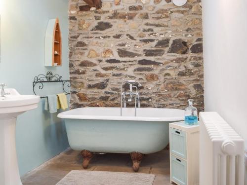 a bathroom with a white tub and a stone wall at Swallow Lodge in Mathry