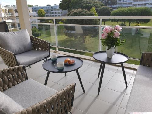 ein Balkon mit zwei Tischen und einer Blumenvase in der Unterkunft Appartement avec grande terrasse dans un magnifique parc à 5 minutes de la plage in La Baule
