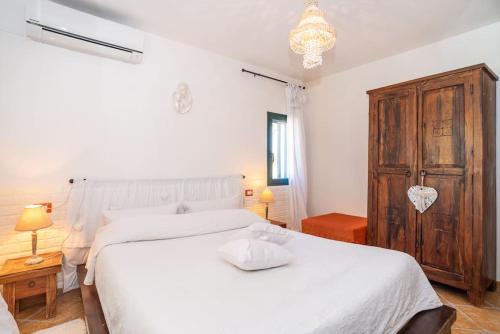 a bedroom with a white bed and a wooden cabinet at Villa Biderrosa in Orosei