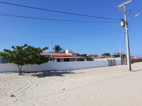 uma parede branca e uma árvore numa rua arenosa em Casa do Kite em Galinhos