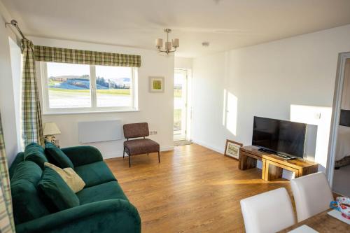 sala de estar con sofá verde y TV en Gardener's Cottage en Alnwick