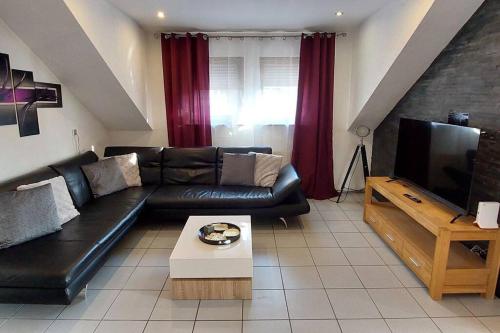 ein Wohnzimmer mit einem schwarzen Ledersofa und einem TV in der Unterkunft 10 Personen Ferienwohnung i. Odw in Mörlenbach