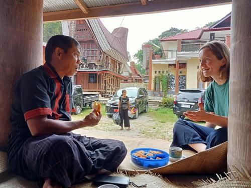 a man and a woman sitting on a porch eating food at NUANSA HOMESTAY Authentic&Hospitality in Rantepao
