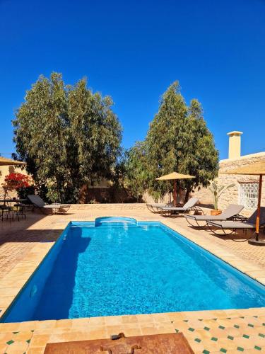 a swimming pool in a yard with chairs and trees at Villa Nouran - Chambre Hôte in Ghazoua