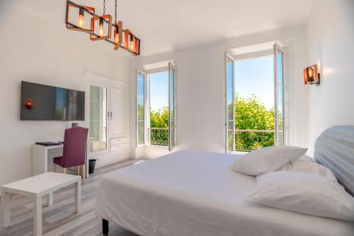 a white bedroom with a bed and a desk and windows at Hotel Les Palmiers in Sainte-Maxime