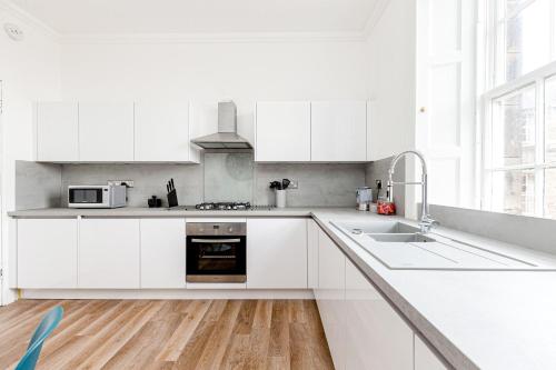 a white kitchen with white cabinets and a sink at Heart of Edinburgh City Centre 3 Bed Georgian Apt in Edinburgh