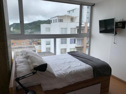 a bed in a room with a large window at Ulivin Apartaestudios Manizales in Manizales