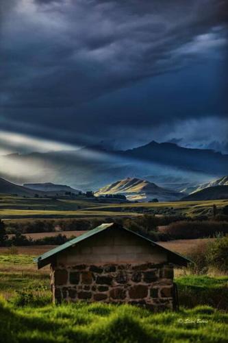 an old building in the middle of a field with mountains at The Stone Barn in Underberg