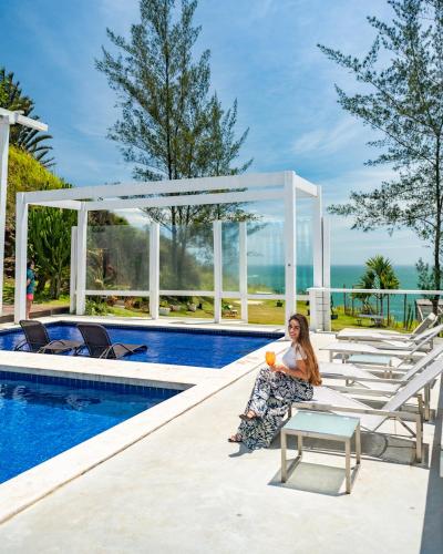 a woman sitting next to a swimming pool at Greco Hotel in Búzios