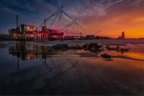 a sunset on the beach with a pier in the water at Old Lighthouse - Beach Apartment - Fiumicino Airport in Fiumicino