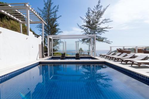 a swimming pool with chairs and the ocean in the background at Greco Hotel in Búzios