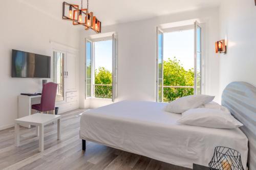 a white bedroom with a bed and a desk and windows at Hotel Les Palmiers in Sainte-Maxime