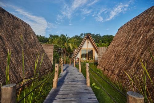 a wooden pathway leading to a hut with thatched roofs at Our Habitas Bacalar - Adults Only in Bacalar