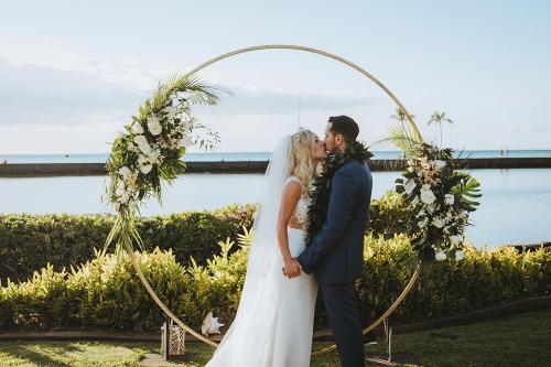 a bride and groom kissing under a wedding arch at Waikoloa Beach Marriott Resort & Spa in Waikoloa