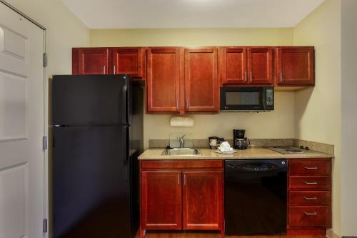a kitchen with wooden cabinets and a black refrigerator at MainStay Suites Fitchburg - Madison in Madison