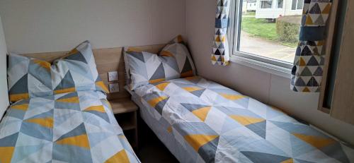 two twin beds in a room with a window at Golden Sands Pine Drive 53, 3 Bedrooms & Wi-fi in Mablethorpe