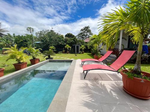 una piscina con 2 sillas rosas junto a una casa en TAHITI - Fare Matavai Hoe en Taravao