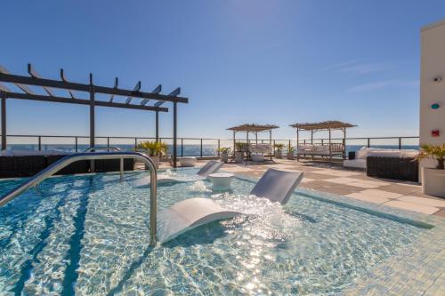 a swimming pool with chairs and the ocean in the background at Modern 4 BR Luxury Condo with Rooftop Pool Next to the Hangout! in Gulf Shores