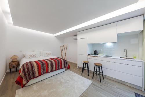 a white bedroom with a bed and a kitchen at Estúdio Cândida, One place … in Nazaré