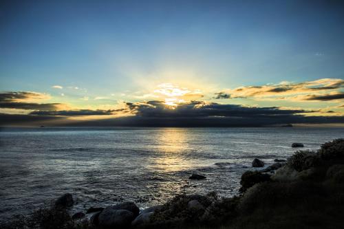 a sunset over a body of water with rocks at Rocklands Seaside Bed and Breakfast in Simonʼs Town
