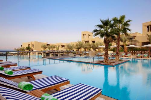 a large swimming pool with lounge chairs and palm trees at Holiday Inn Resort Dead Sea, an IHG Hotel in Sowayma