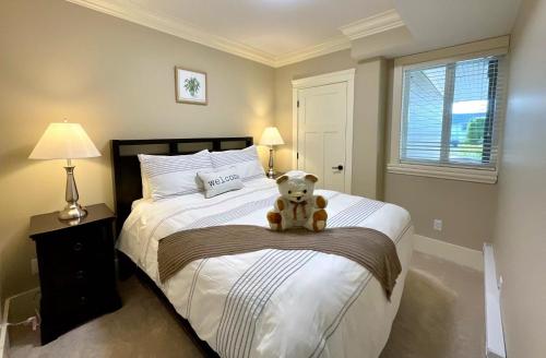 un osito de peluche sentado en una cama en un dormitorio en New two-bedroom legal suite with parking, en White Rock
