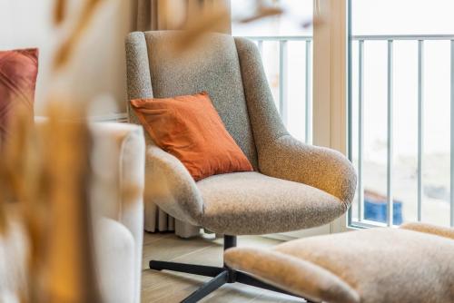 una almohada naranja sentada en una silla junto a una ventana en Seagusta - sea view apartment in Middelkerke, en Middelkerke