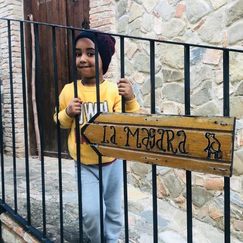 a young boy standing behind a gate with a sign at La Magara in Civita